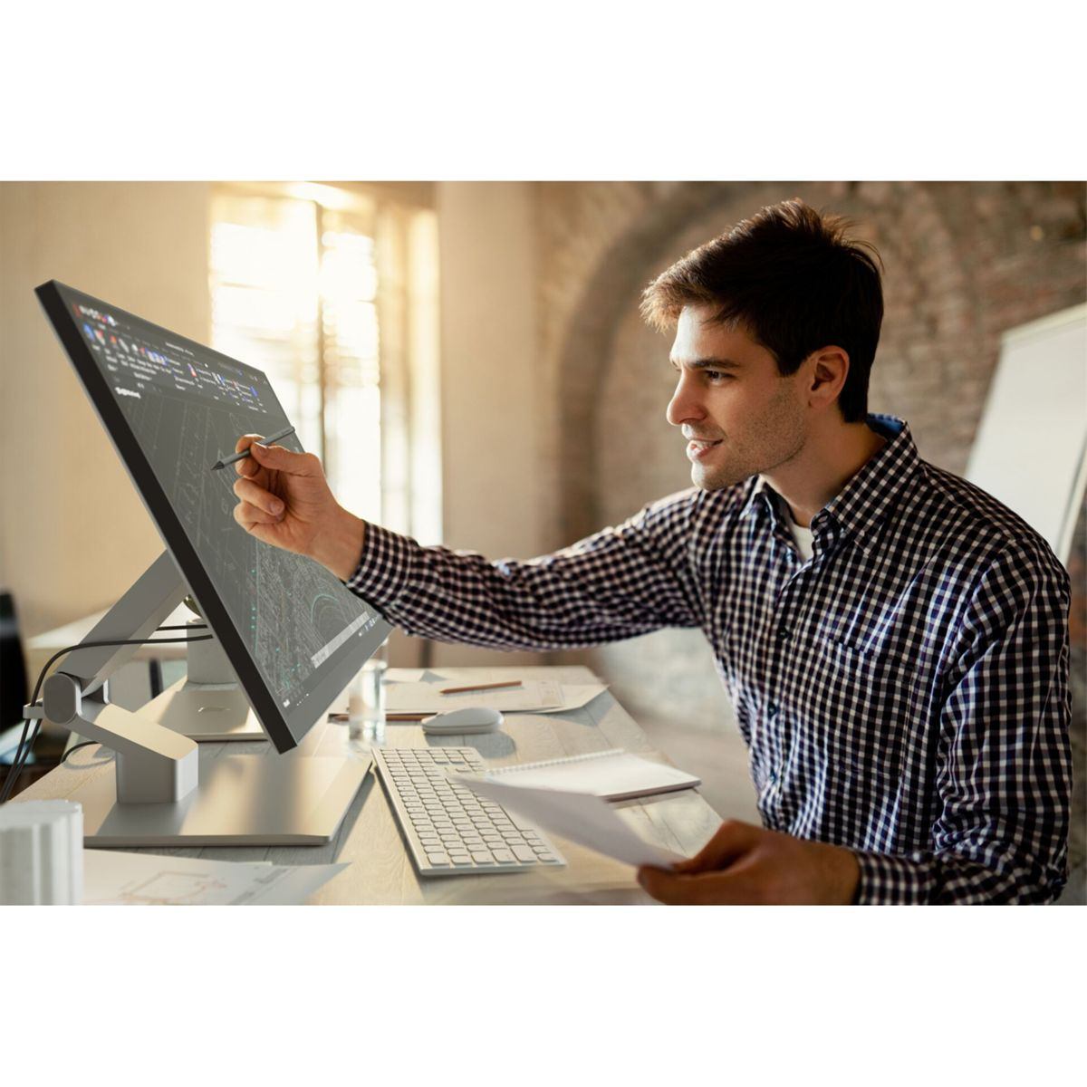 Un uomo con camicia a scacchi lavora su un monitor touchscreen con uno stilo.