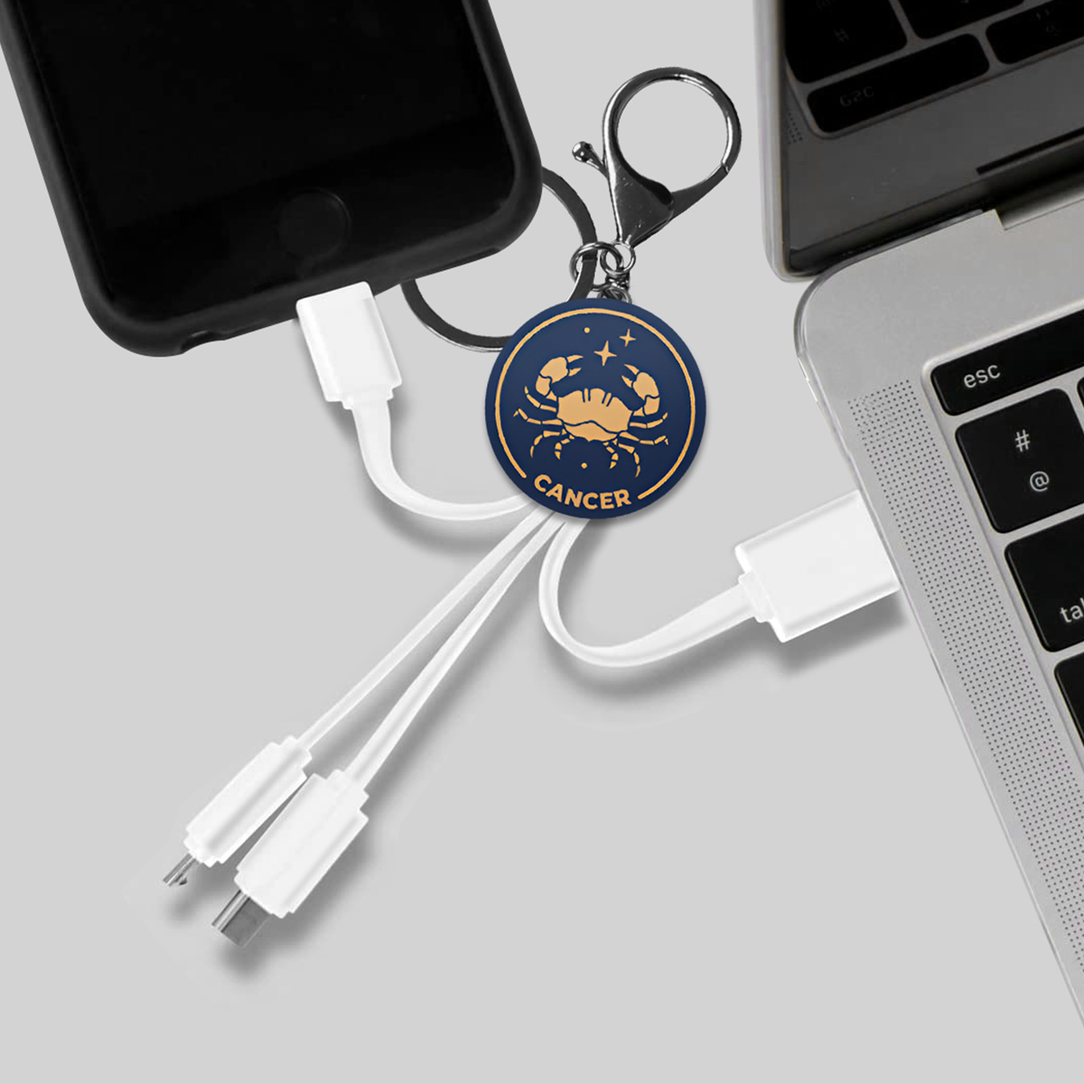 Un porte-clés signe du zodiaque Cancer avec des câbles de chargement connectés à un téléphone et un ordinateur portable.