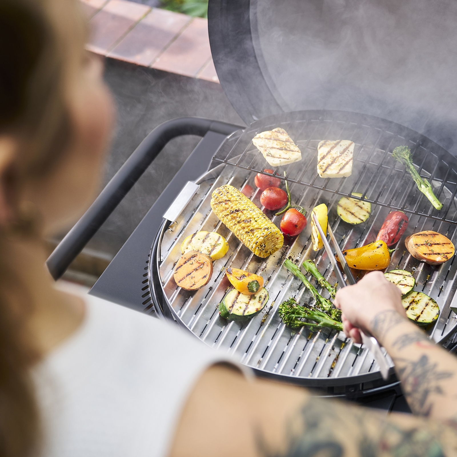 Gemüse und Halloumi werden auf einem Grill zubereitet, Dampf steigt auf.