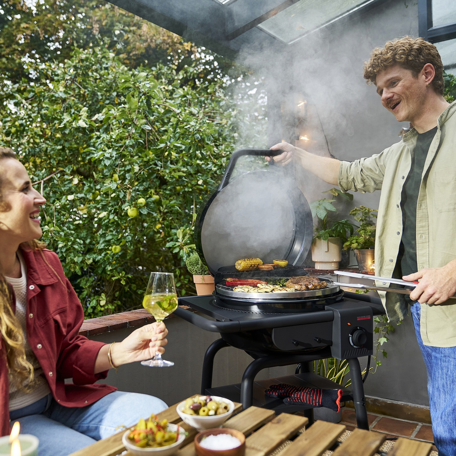 Mann und Frau grillen auf einer Terrasse mit Wein und Essen.