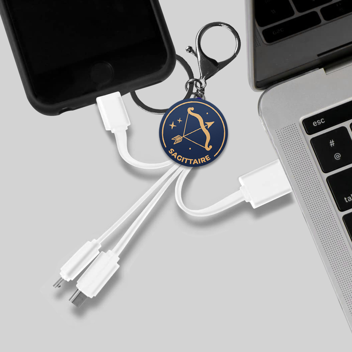 Un ciondolo zodiacale del Sagittario è attaccato a un cavo di ricarica collegato a un telefono e a un laptop.