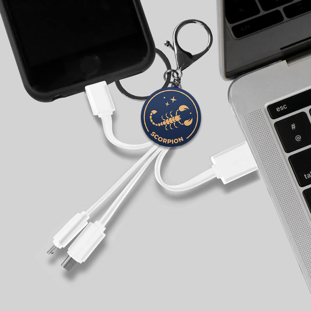Un portachiavi con ciondolo a forma di scorpione con cavi di ricarica collegati a un telefono e un laptop.