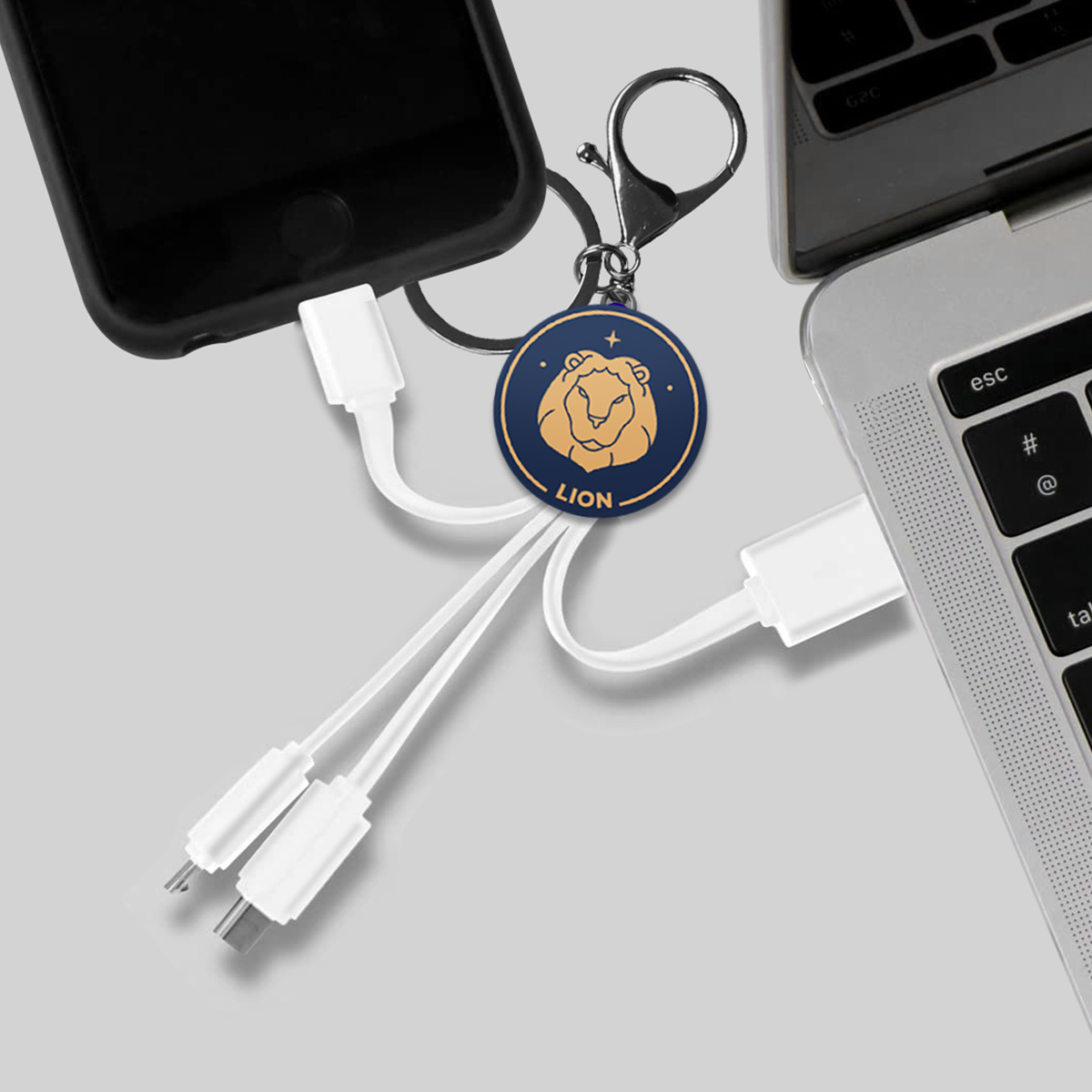 Un cavo di ricarica con un ciondolo a forma di leone è collegato a uno smartphone e a un laptop.