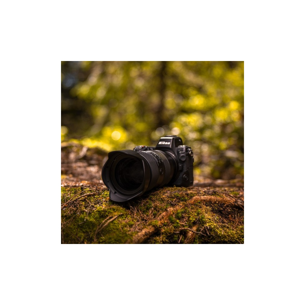 Czarny aparat Nikon leży na omszałym leśnym podłożu.