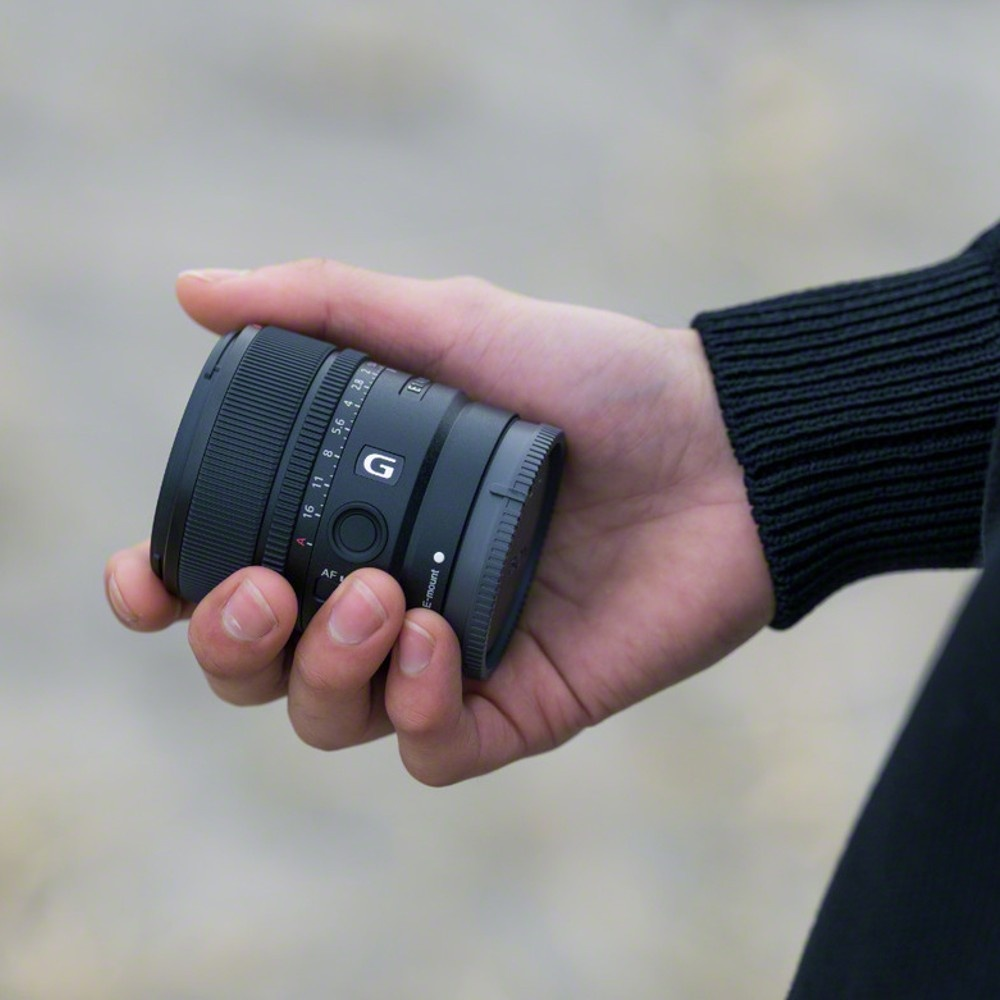 Dłoń trzyma mały, czarny obiektyw aparatu z logo G.