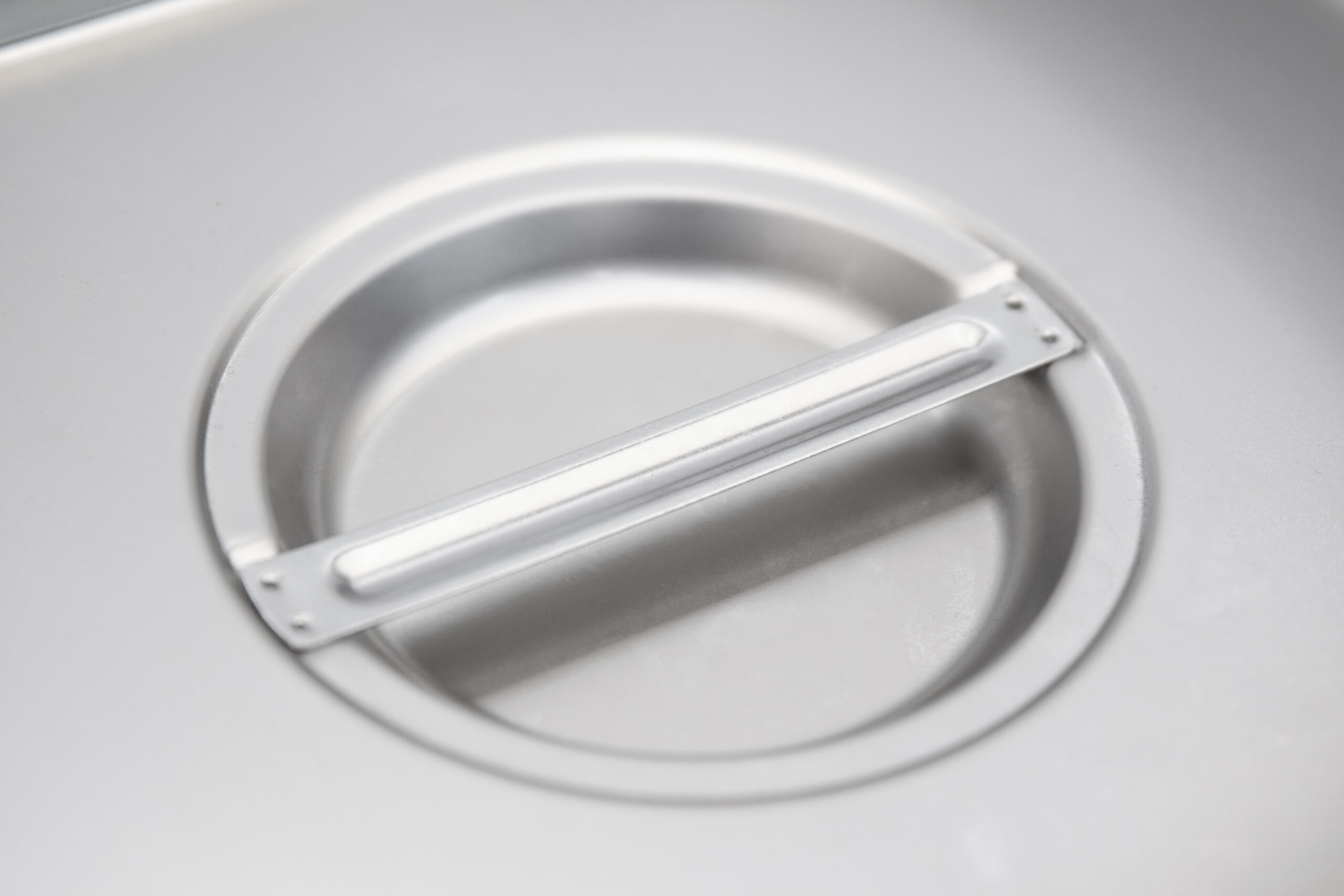 Close-up of a silver metal container with a circular insert and a handle.