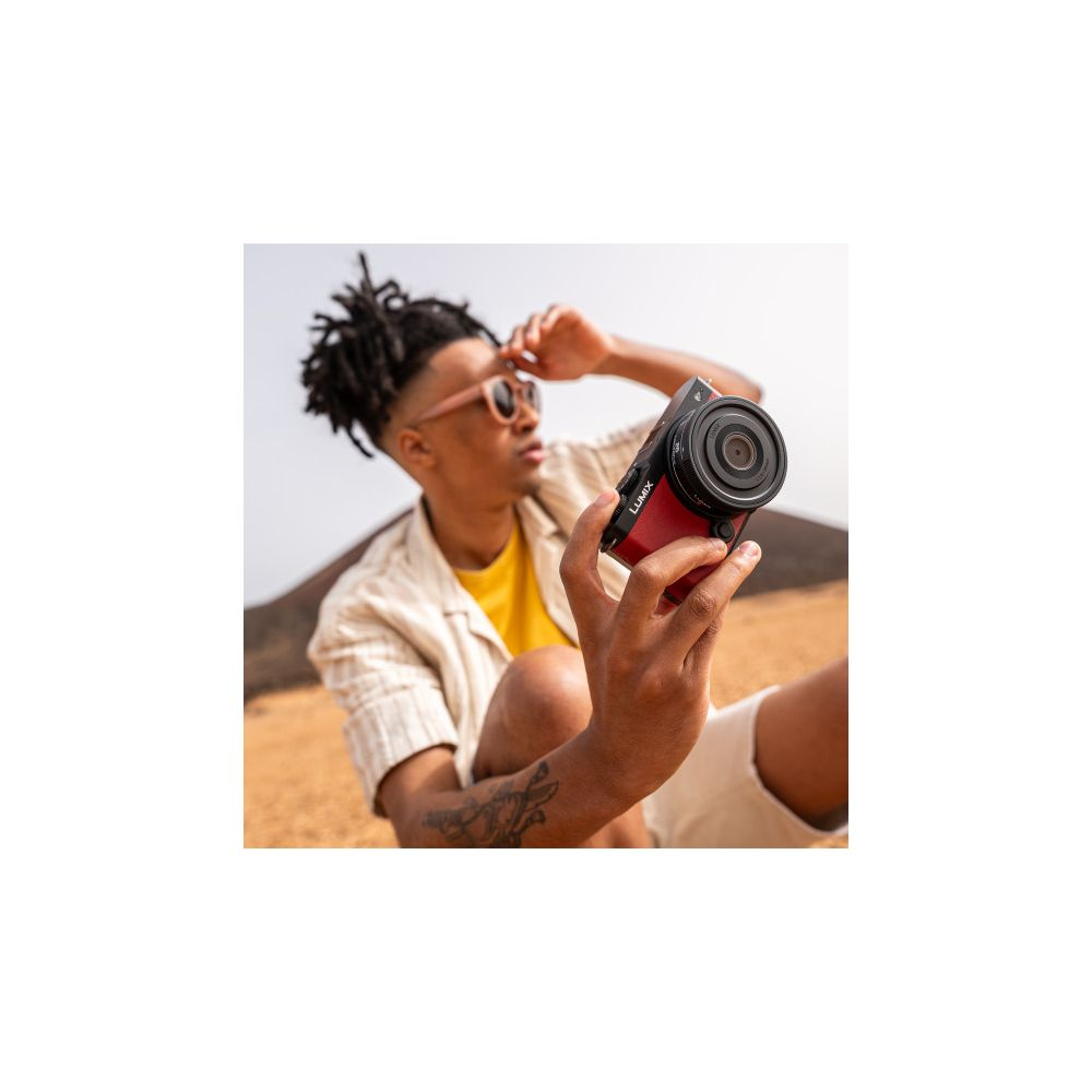 Mann mit Dreadlocks und Sonnenbrille hält eine rote Kamera in einer Wüstenlandschaft.