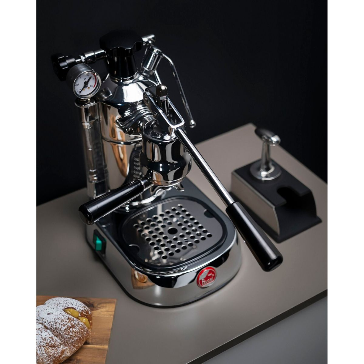 Glänzende Chrom-Espressomaschine mit schwarzen Griffen und Manometer. Links ein Croissant.