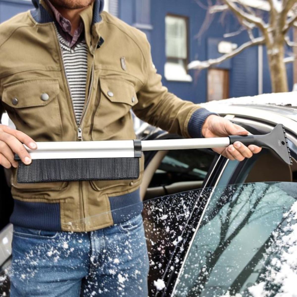 Man gebruikt sneeuwborstel om auto schoon te maken in winter.