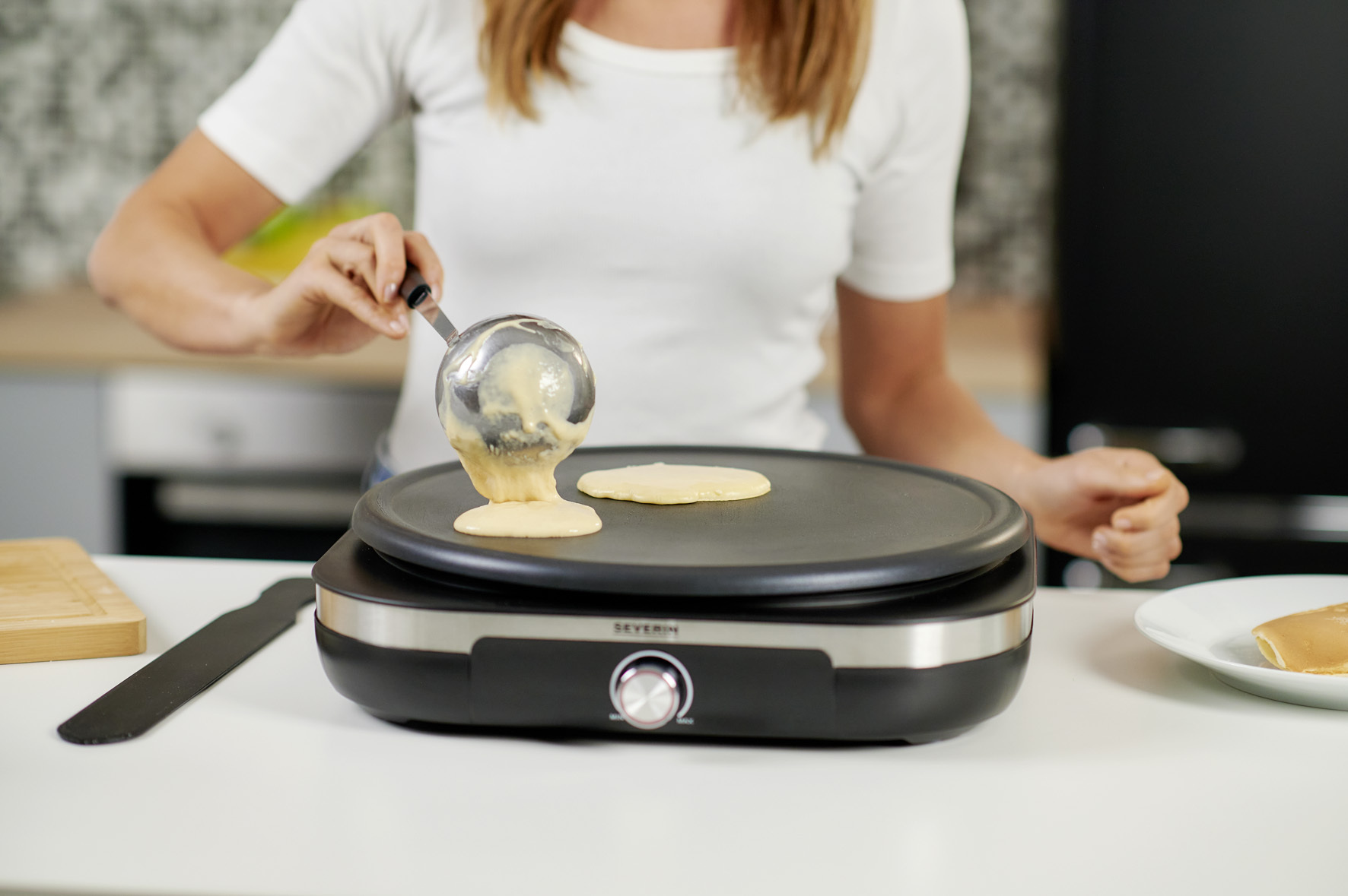 Osoba nalewa ciasto z chochli na płytę do robienia naleśników.