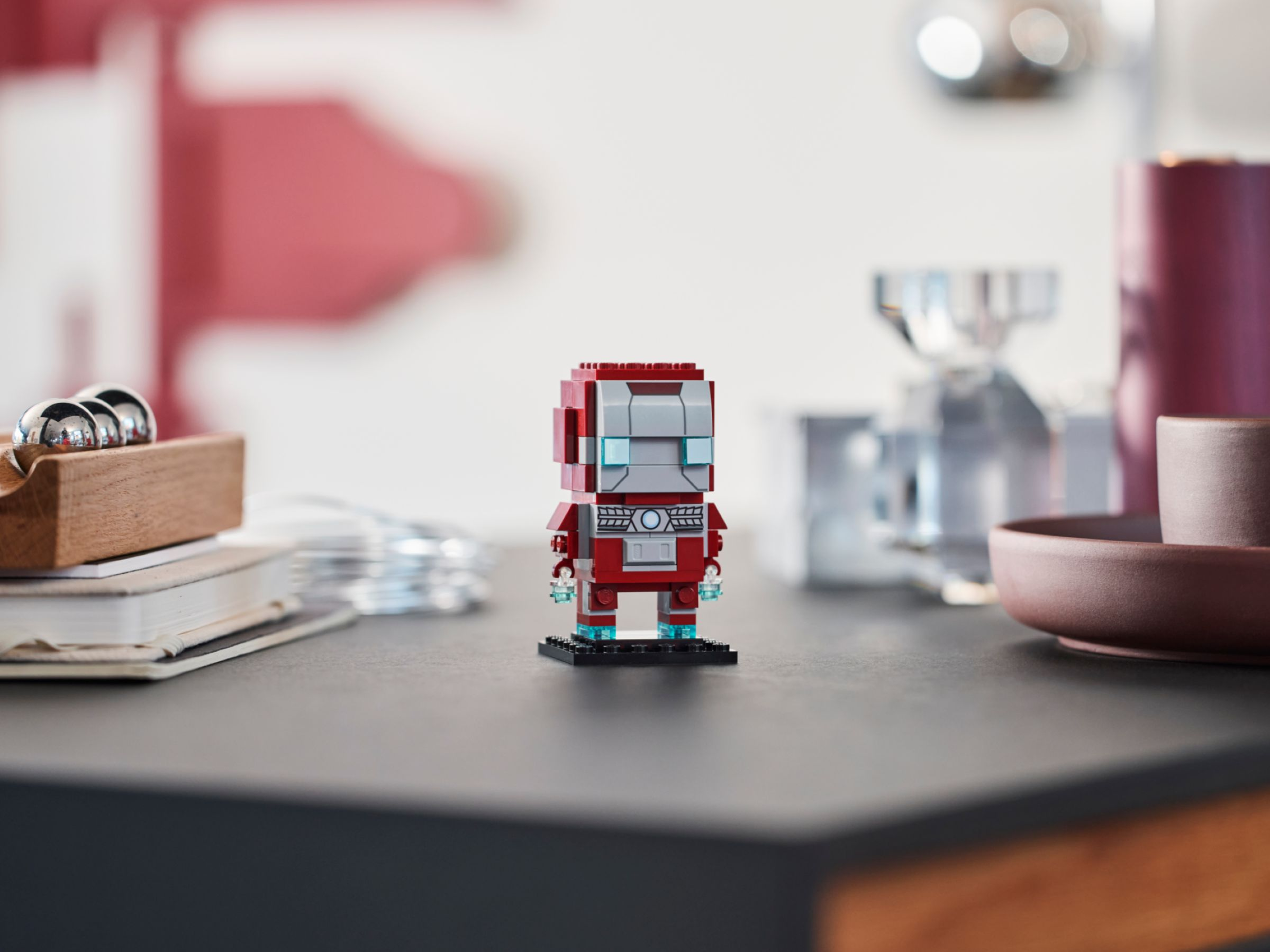 Kırmızı Lego Iron Man figürü siyah bir zeminde duruyor. Arkada bulanık nesneler var.
