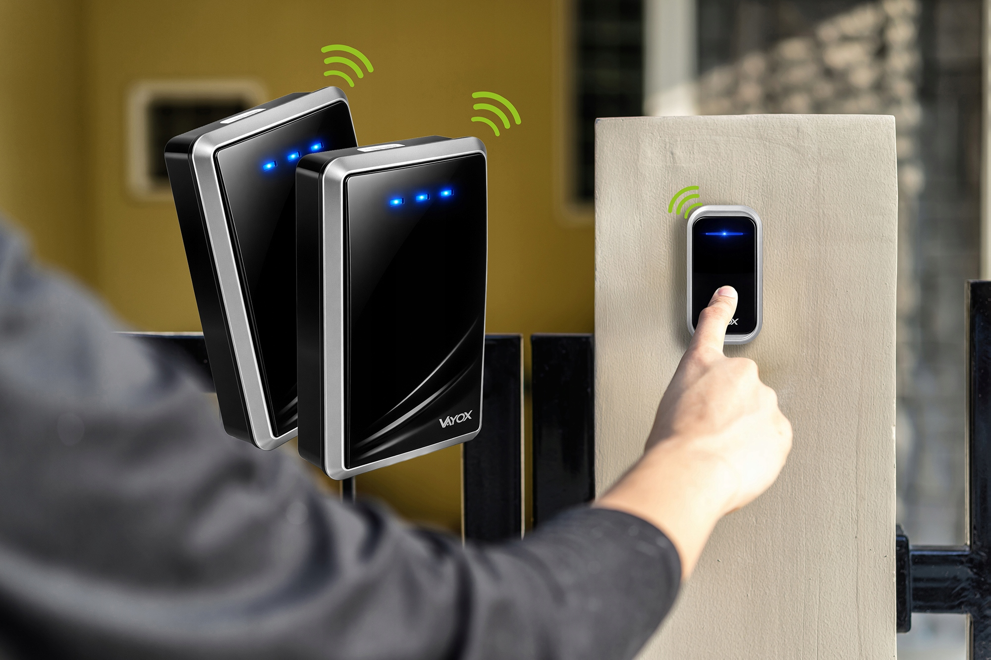 Palec naciska dzwonek do drzwi na słupku. Dwa nadajniki po lewej.