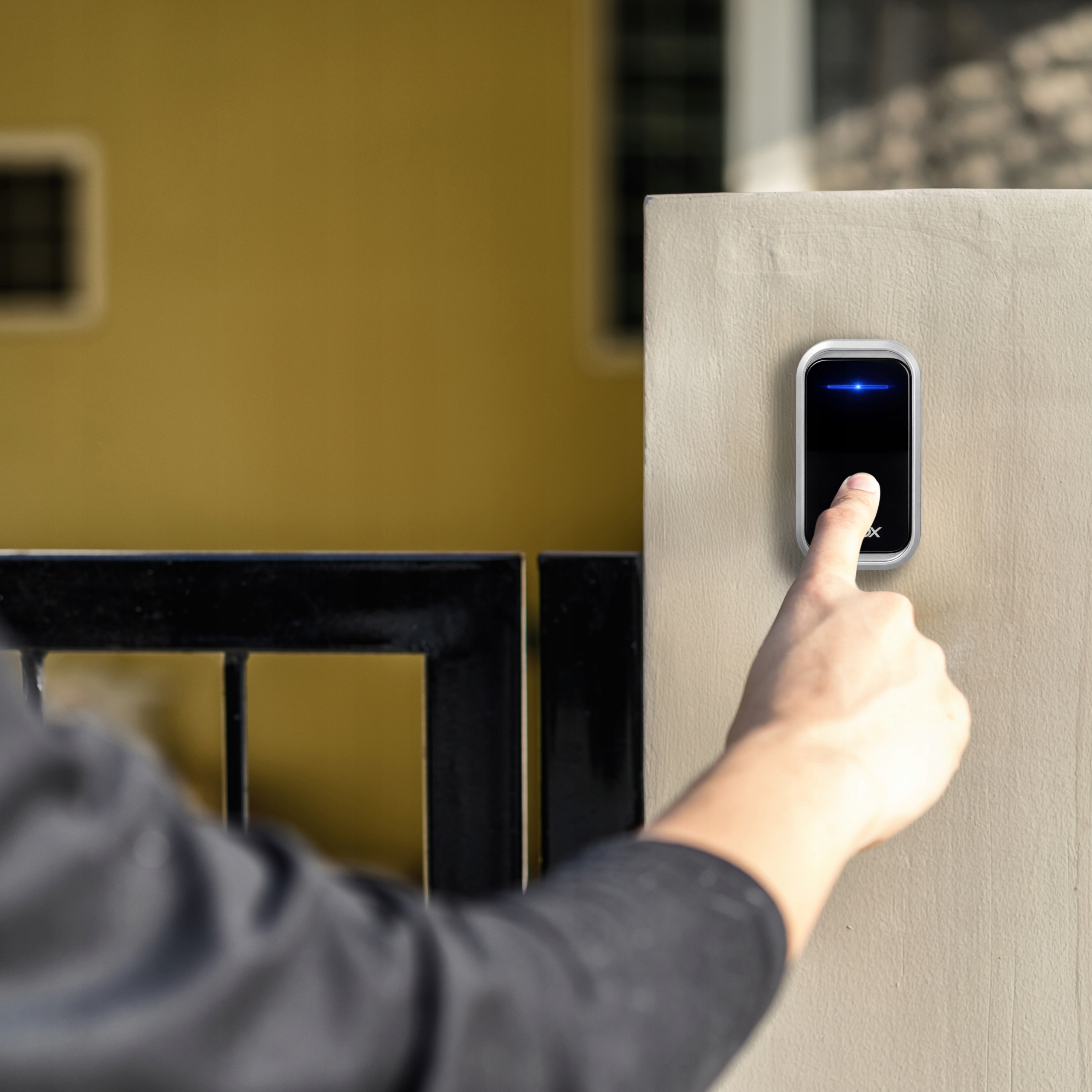 Palec naciska dzwonek do drzwi na ścianie, obok bramy.