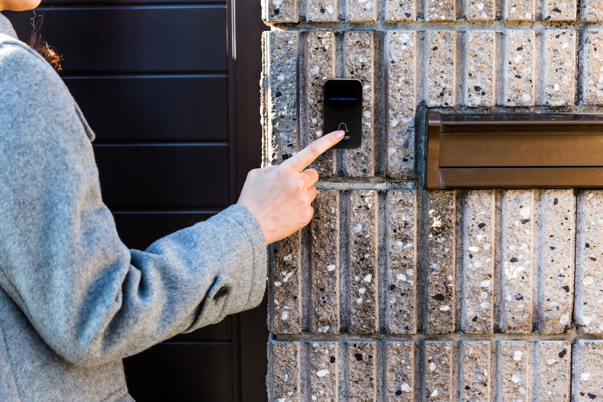 Dłoń w szarym płaszczu naciska dzwonek na kamiennej fasadzie.