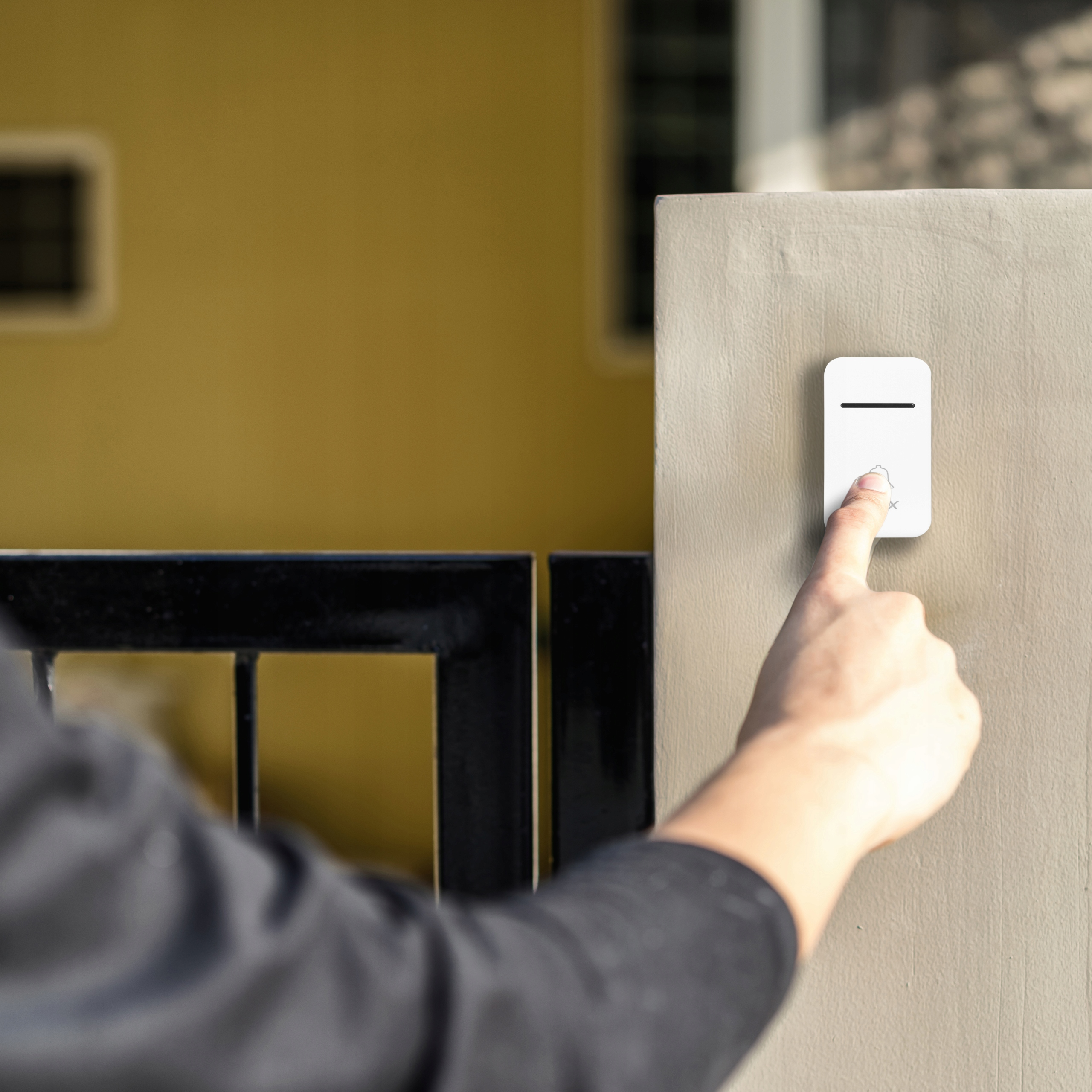 Palec naciska biały dzwonek do drzwi na ścianie.