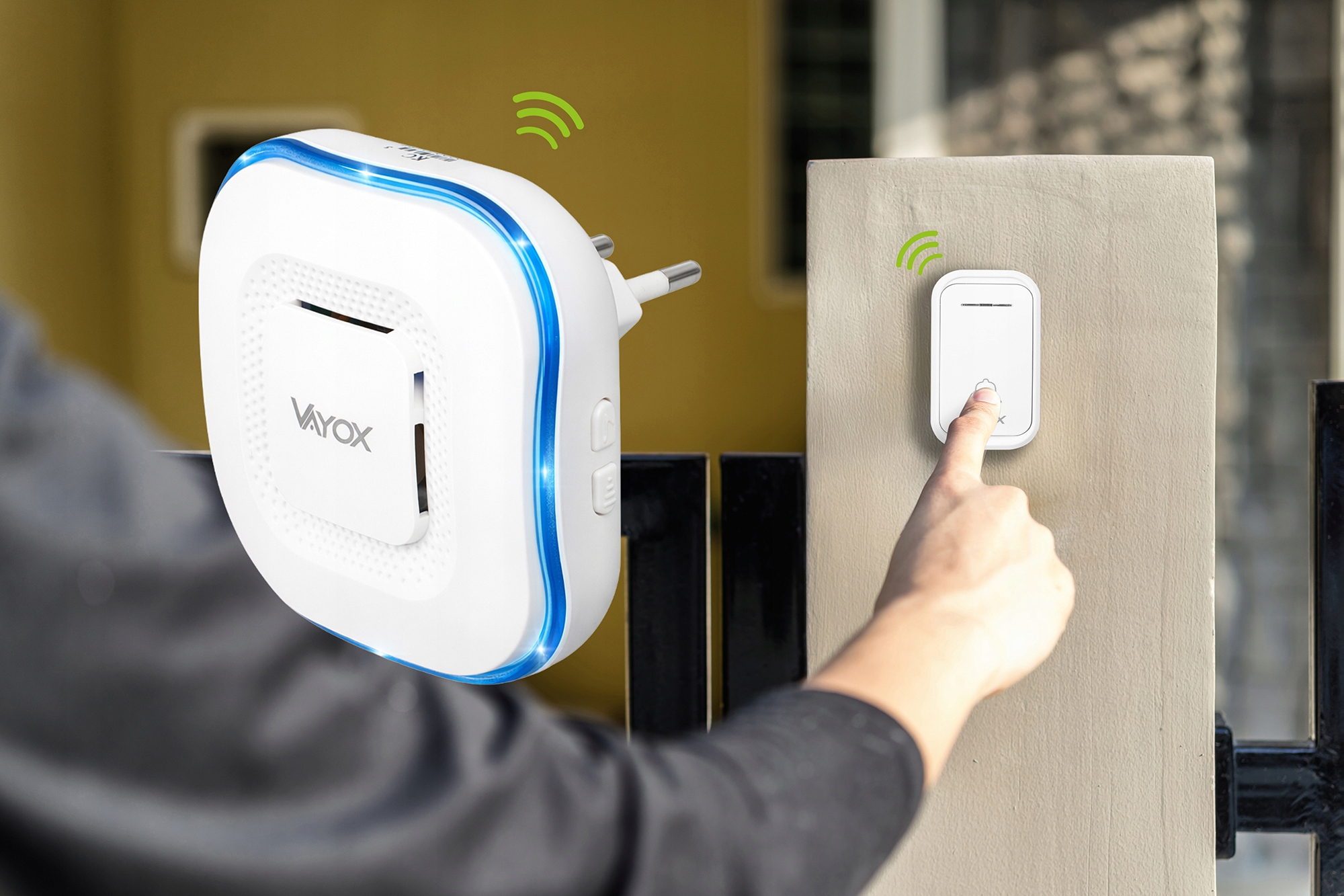 Palec naciska biały przycisk dzwonka do drzwi na ścianie. W pobliżu znajduje się biała wtyczka z niebieskimi światłami.