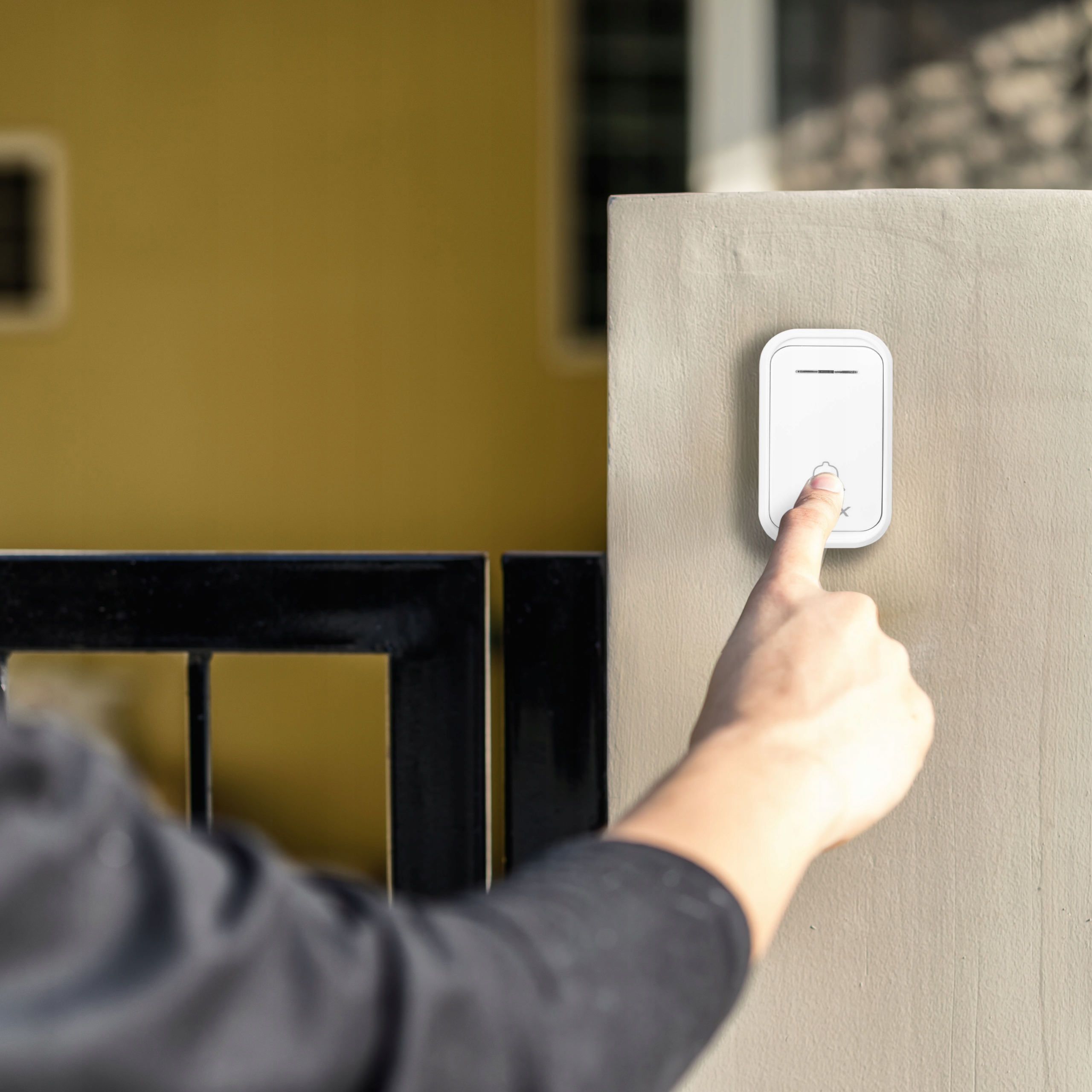 Palec naciska biały dzwonek do drzwi na ścianie obok bramy.