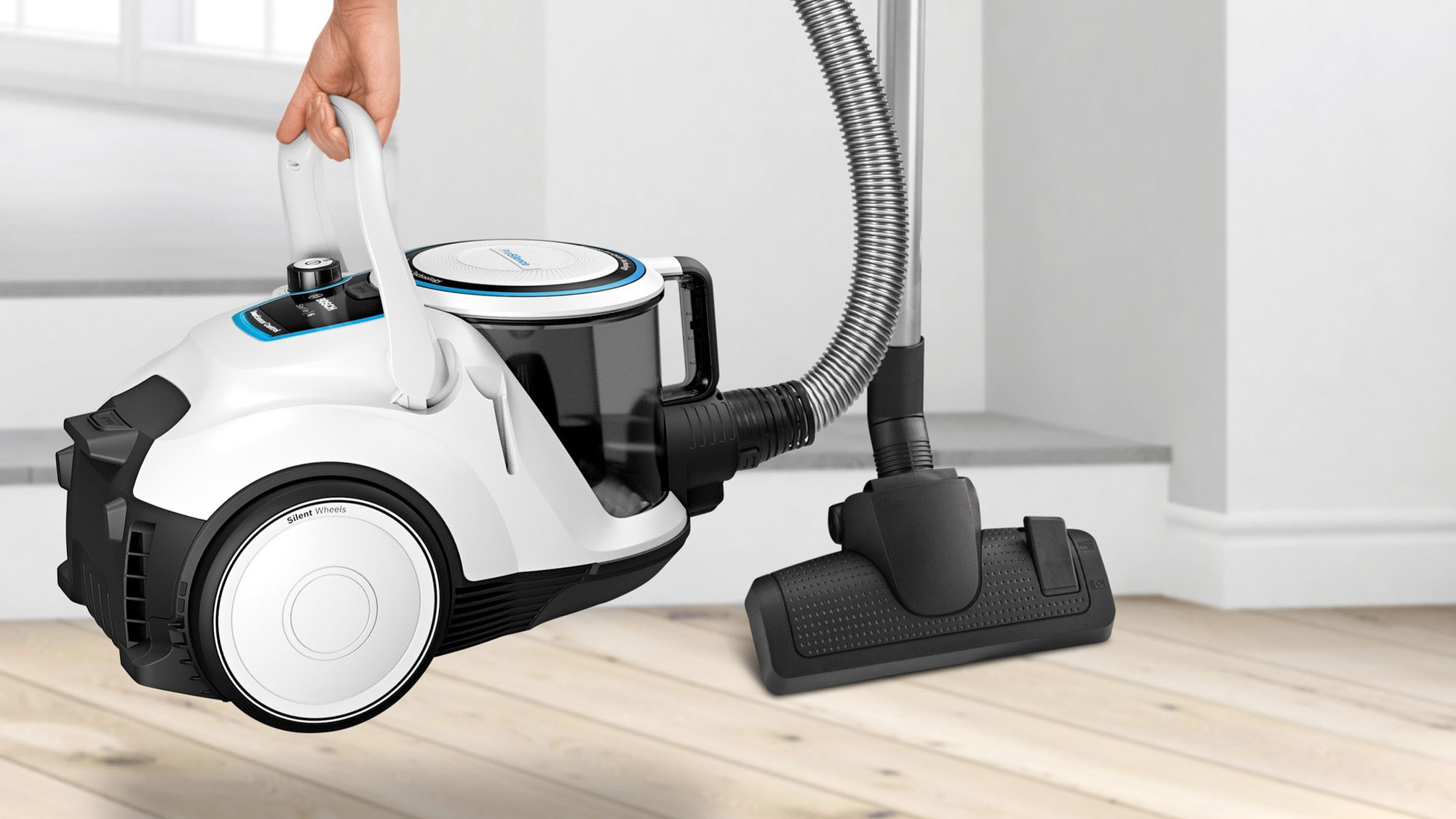 Ręka podnosi biało-czarny odkurzacz z wężem i szczotką.