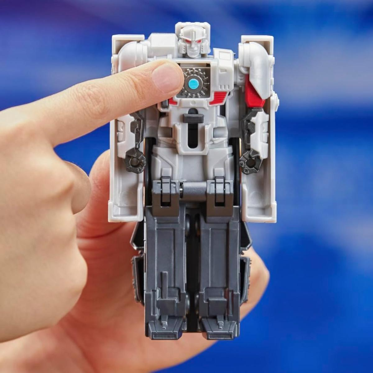 Una mano sostiene un juguete Transformer gris y blanco con detalles azules sobre fondo azul.