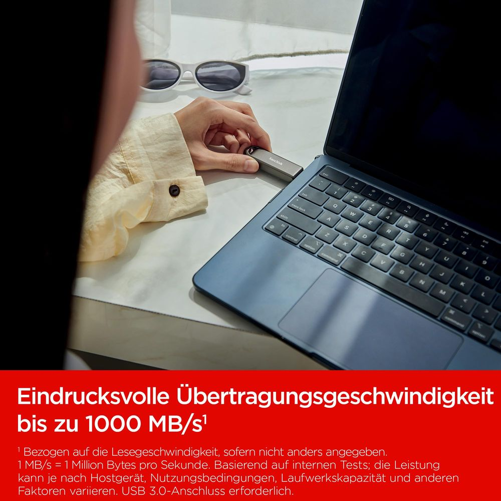 Una mano inserisce una chiavetta USB in un laptop. Occhiali da sole bianchi nelle vicinanze.