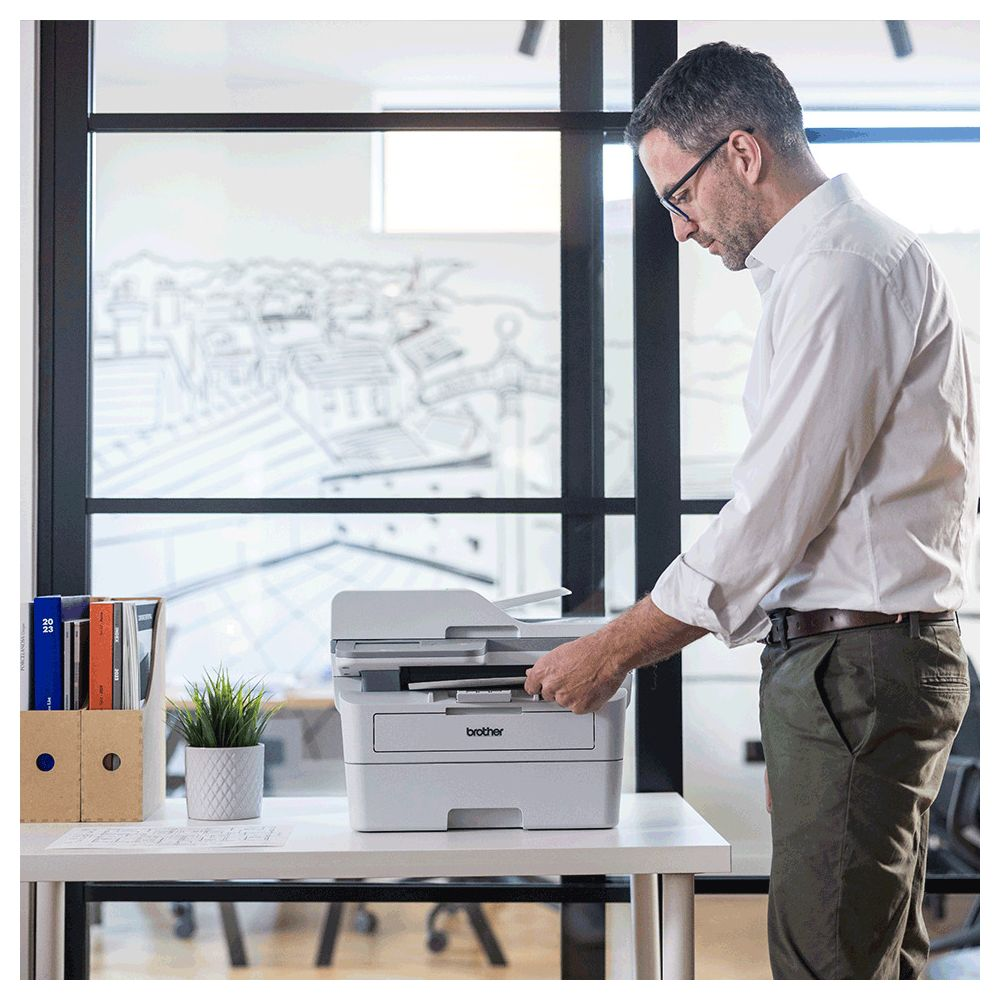Homme en chemise blanche utilise une imprimante dans un bureau. Dossiers et plante sur bureau.