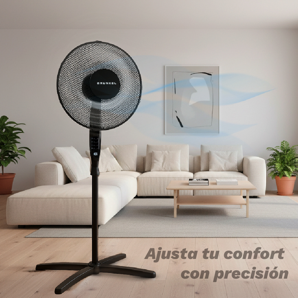 Un ventilador de pie negro en una sala de estar luminosa con un sofá.