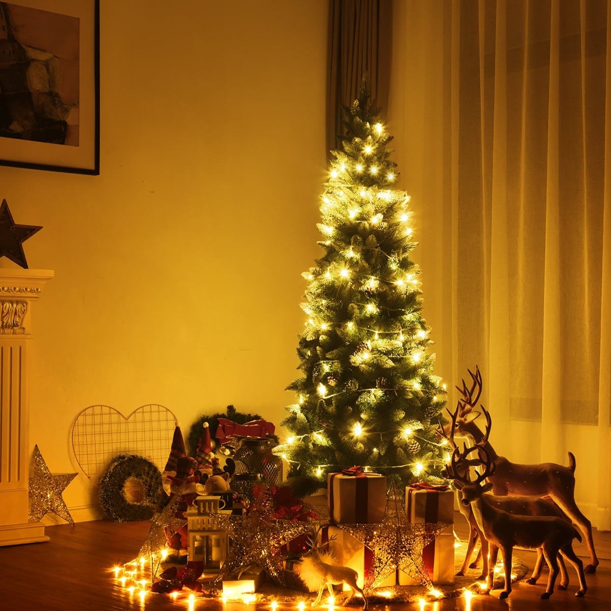 Een verlichte kerstboom met cadeaus, rendierfiguren en decoraties.