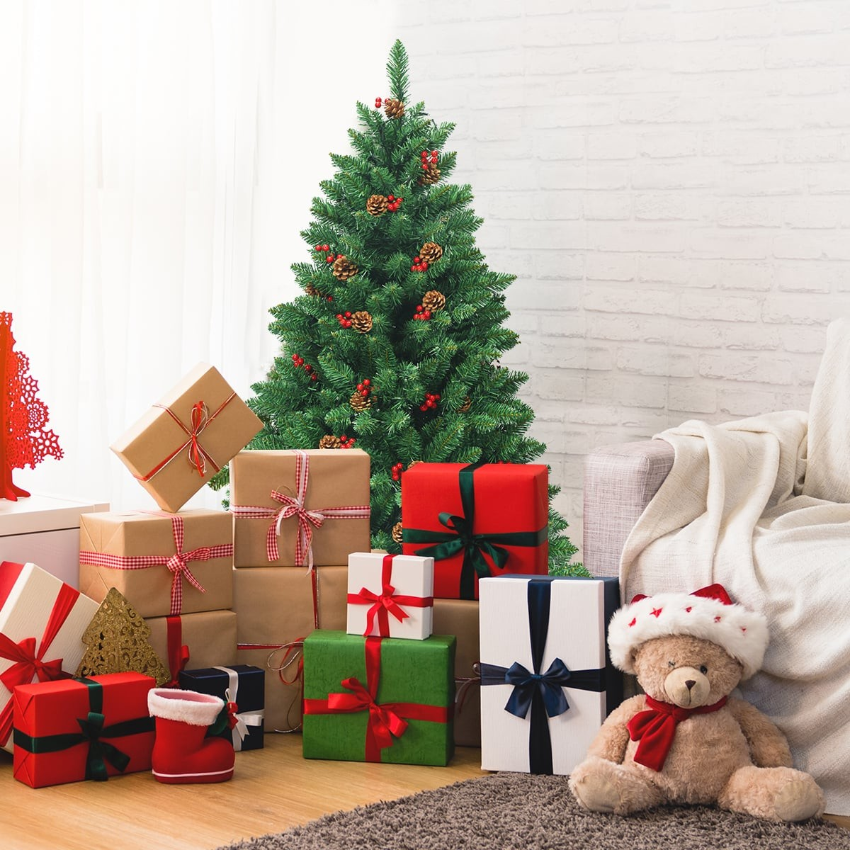 Een teddybeer met kerstmuts zit naast cadeaus en een kerstboom.