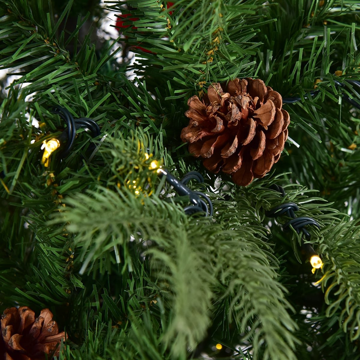 Close-up van een kerstboom met dennenappels en lampjes.