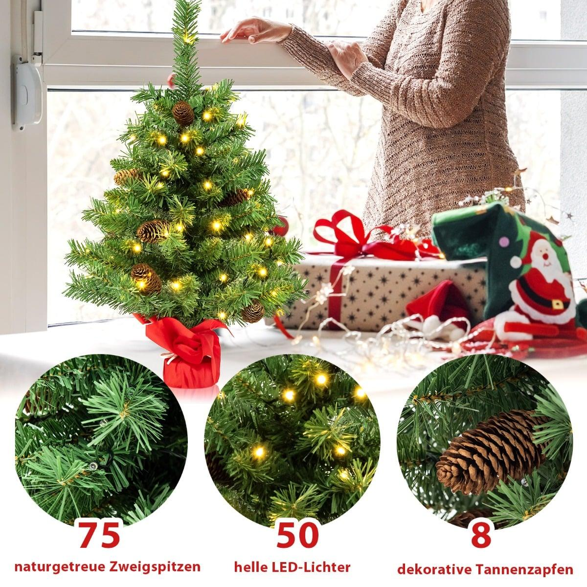 Een kleine kerstboom met lampjes, dennenappels en een vrouw op de achtergrond.