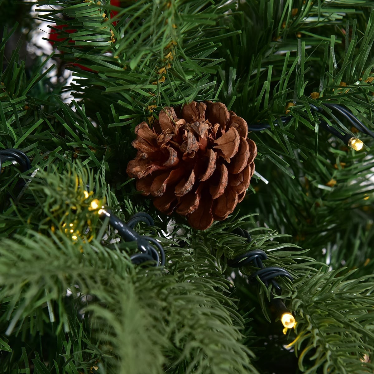 Een dennenappel hangt aan een groene kerstboom met lichtslingers.