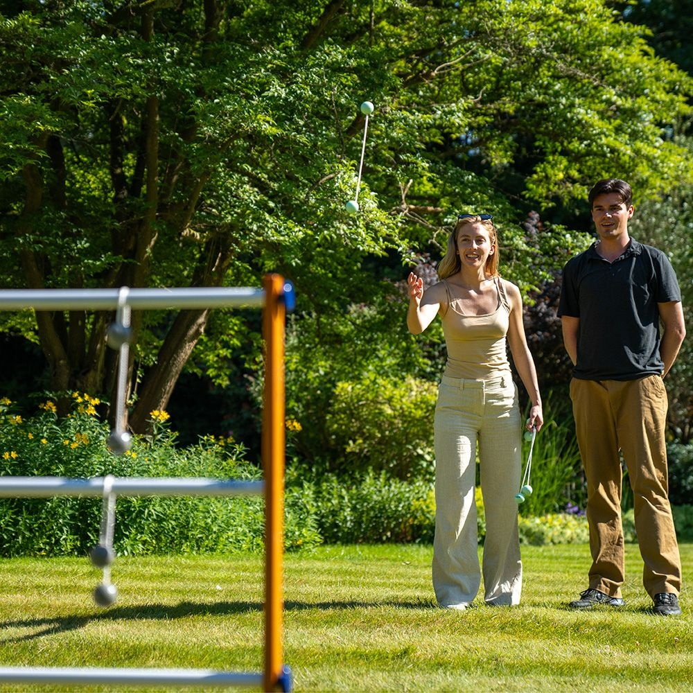 Mann und Frau spielen im Garten mit Bällen, ein Spielgerät im Vordergrund.