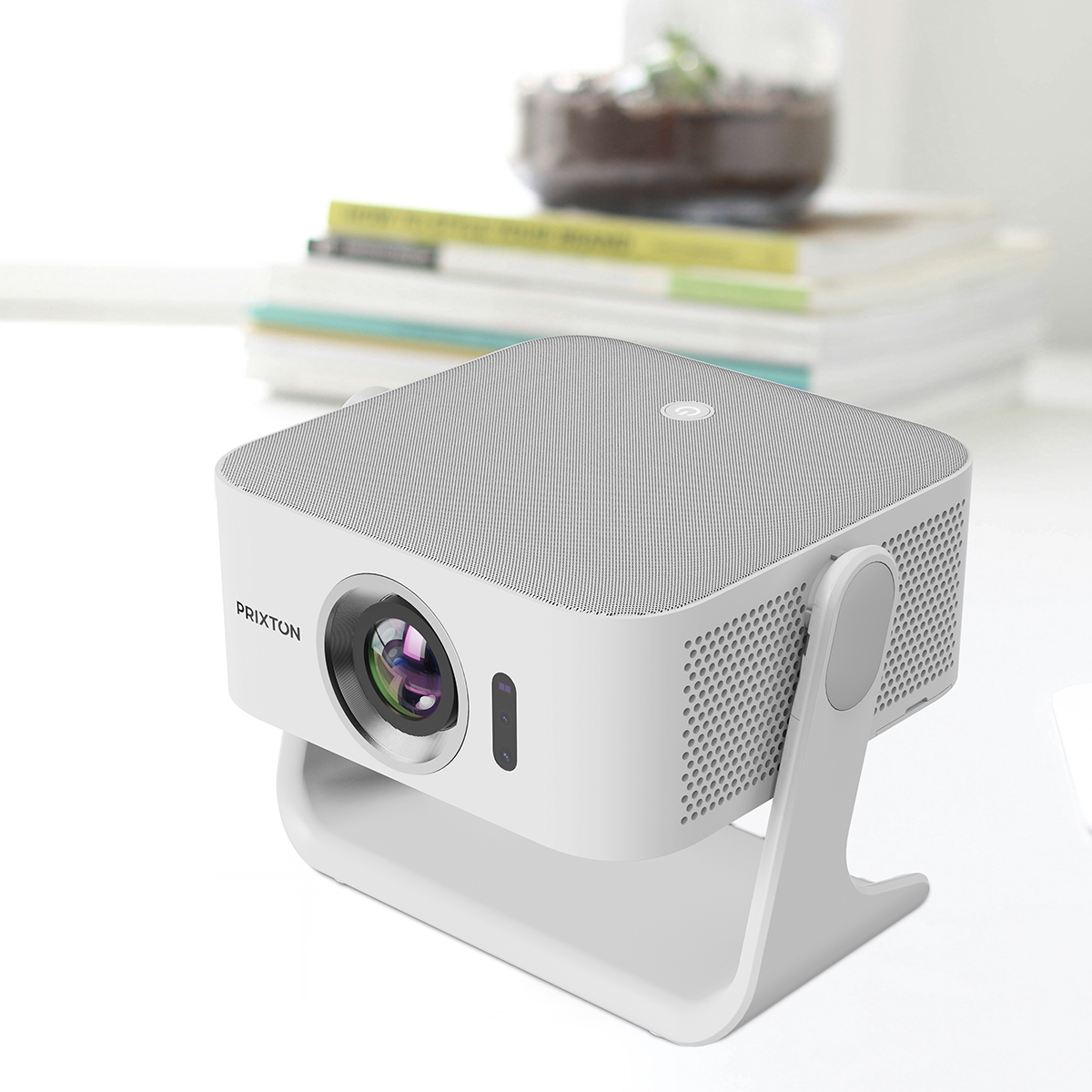 Biały projektor Prixton stoi na stojaku, z książkami i rośliną w tle.