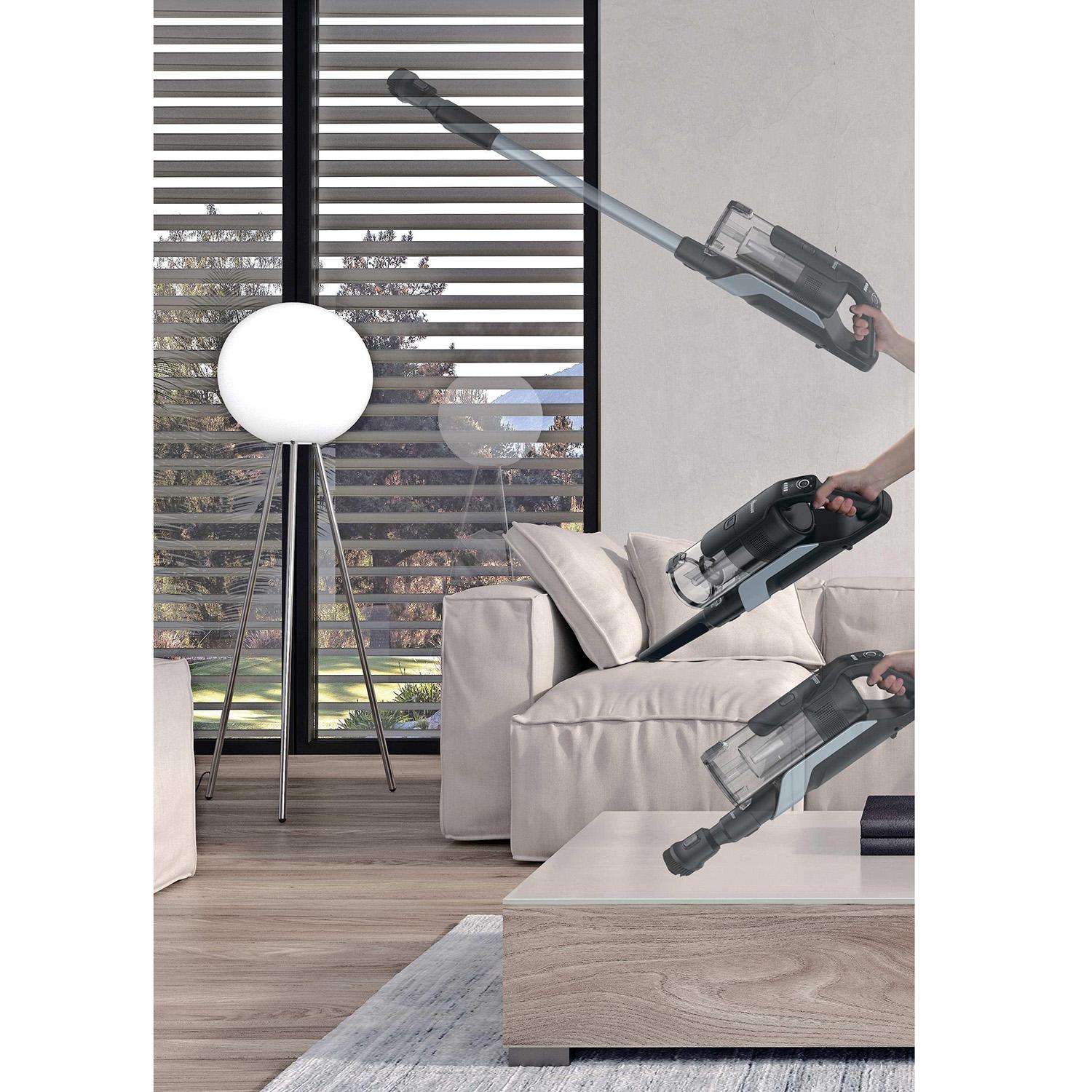 Een draadloze stofzuiger in actie in een woonkamer met bank en lamp.