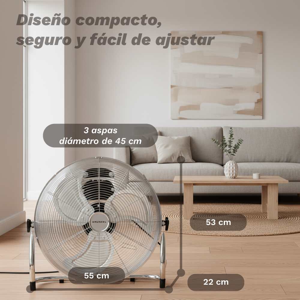 Un ventilador de suelo plateado está en primer plano, junto a un sofá y una mesa.