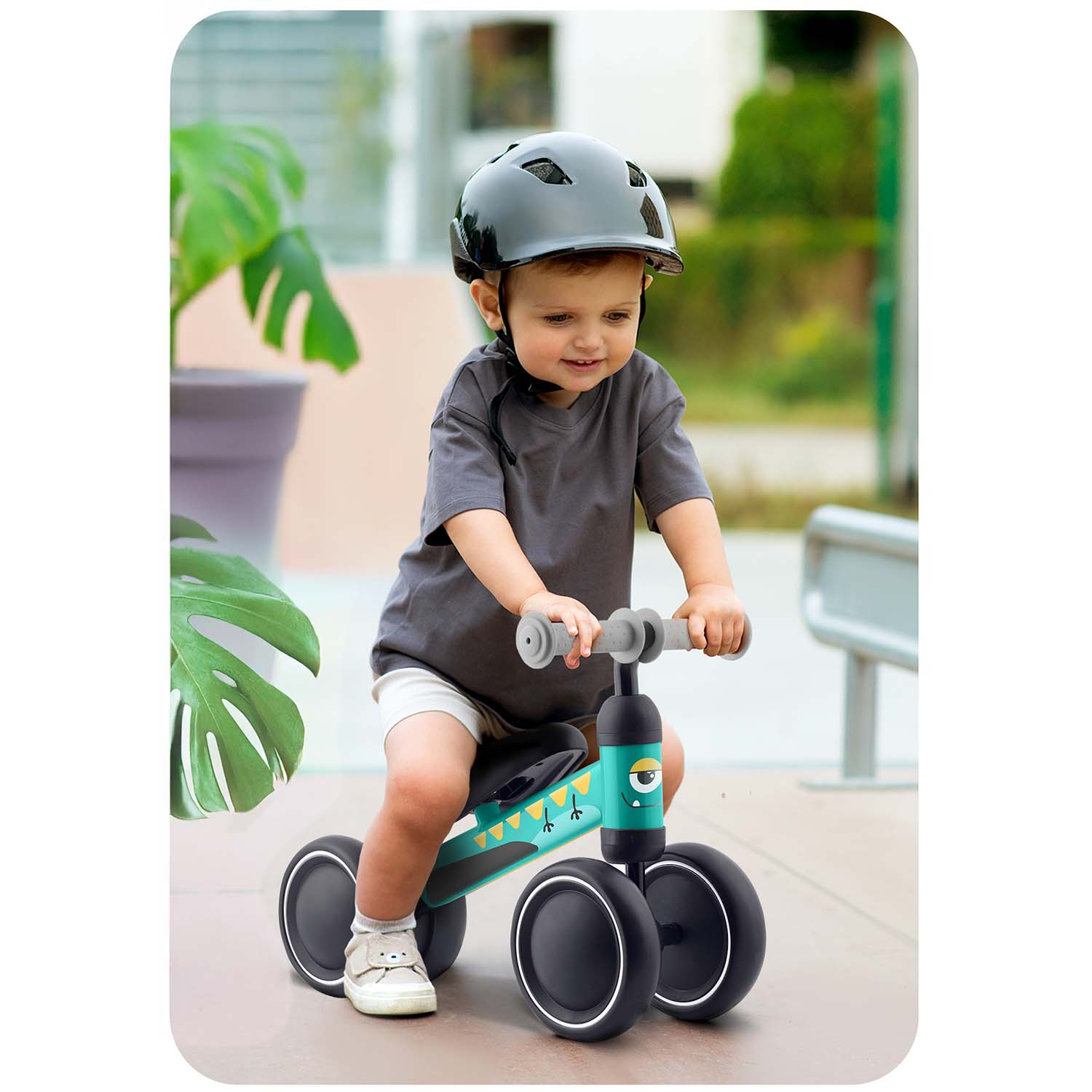 Dziecko w kasku jeździ na turkusowym rowerku biegowym z motywem potwora na zewnątrz.