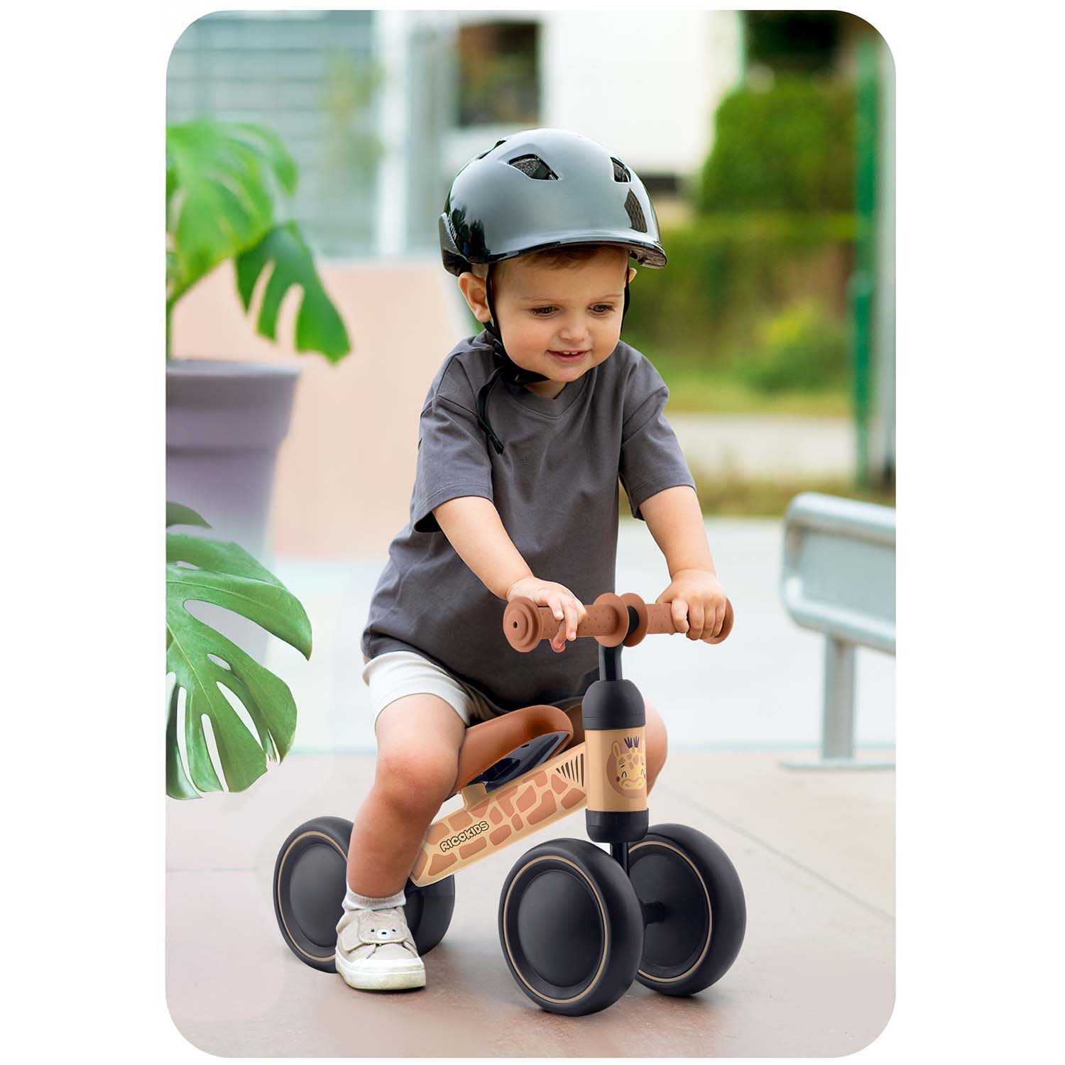 Maluch w kasku jedzie rowerkiem biegowym z motywem żyrafy na zewnątrz.