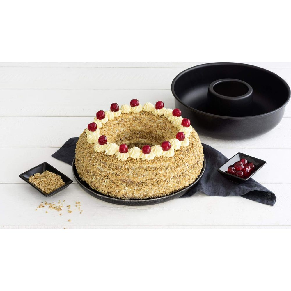 Ein Kranzkuchen mit Nüssen, Sahnetupfern und Kirschen neben einer Kuchenform.