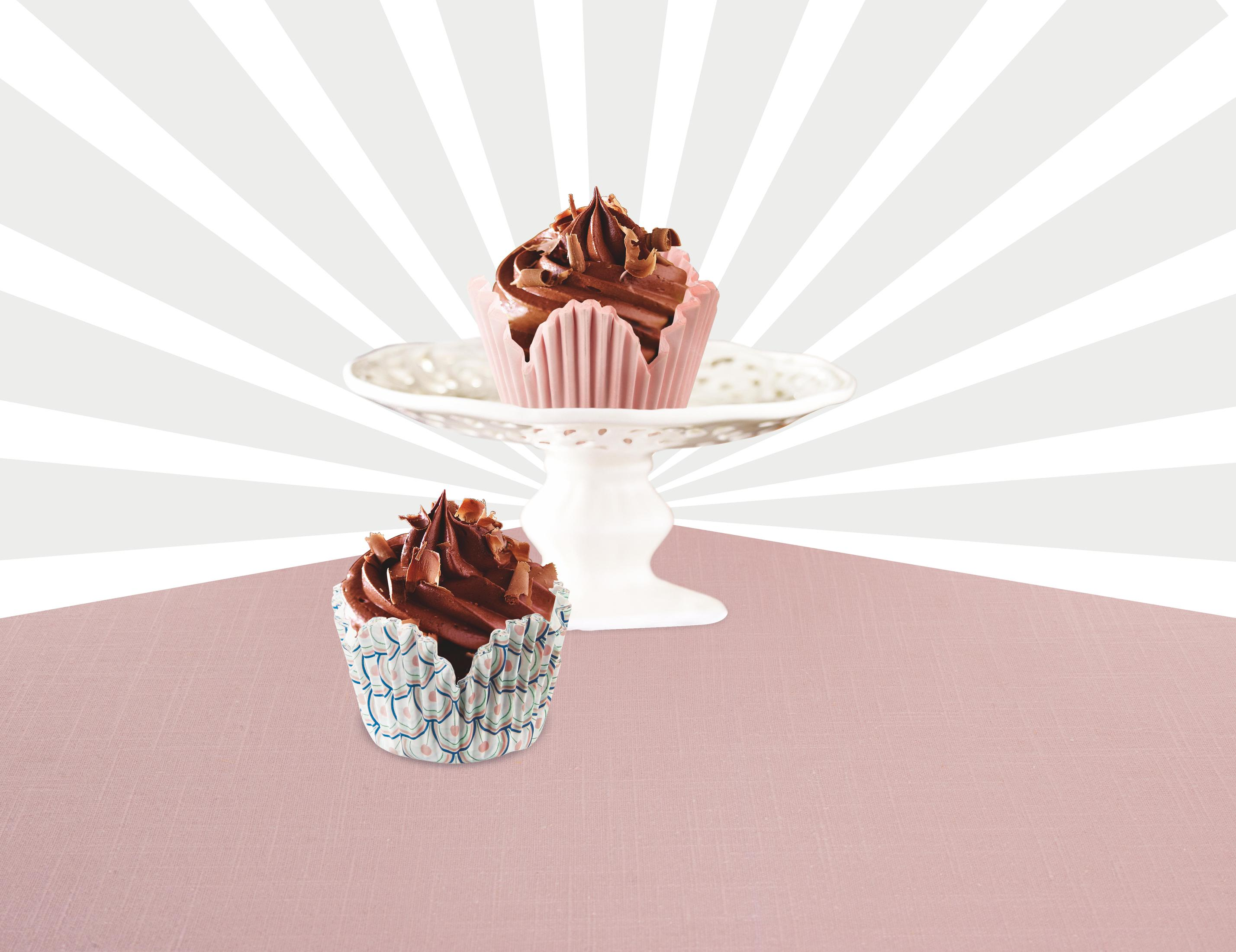 Zwei Schokoladen-Cupcakes mit Rosafarbenem und blauem Muster auf rosa Unterlage.