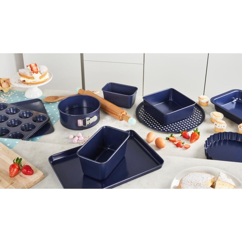 Dunkelblaue Backformen, Kuchen, Erdbeeren und Eier auf einer Tischplatte.
