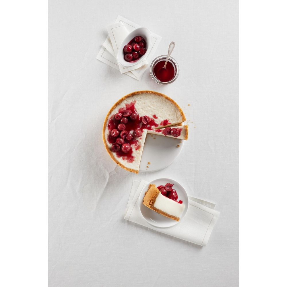 Gâteau au fromage avec des cerises et une part sur une assiette, avec un bol de cerises à proximité.