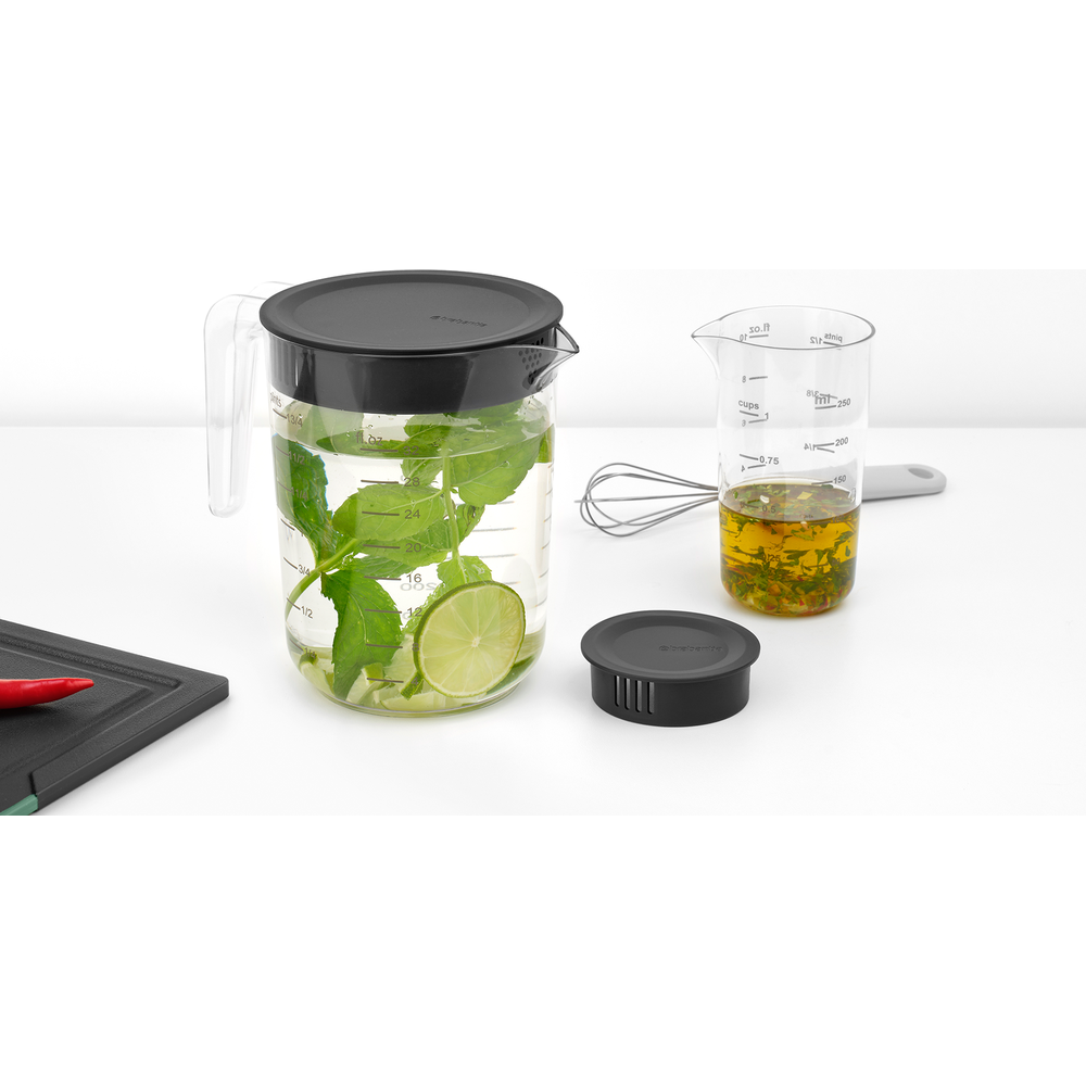 Ein Glas Krug mit Minze und Limettenscheiben, daneben ein Messbecher mit Dressing.