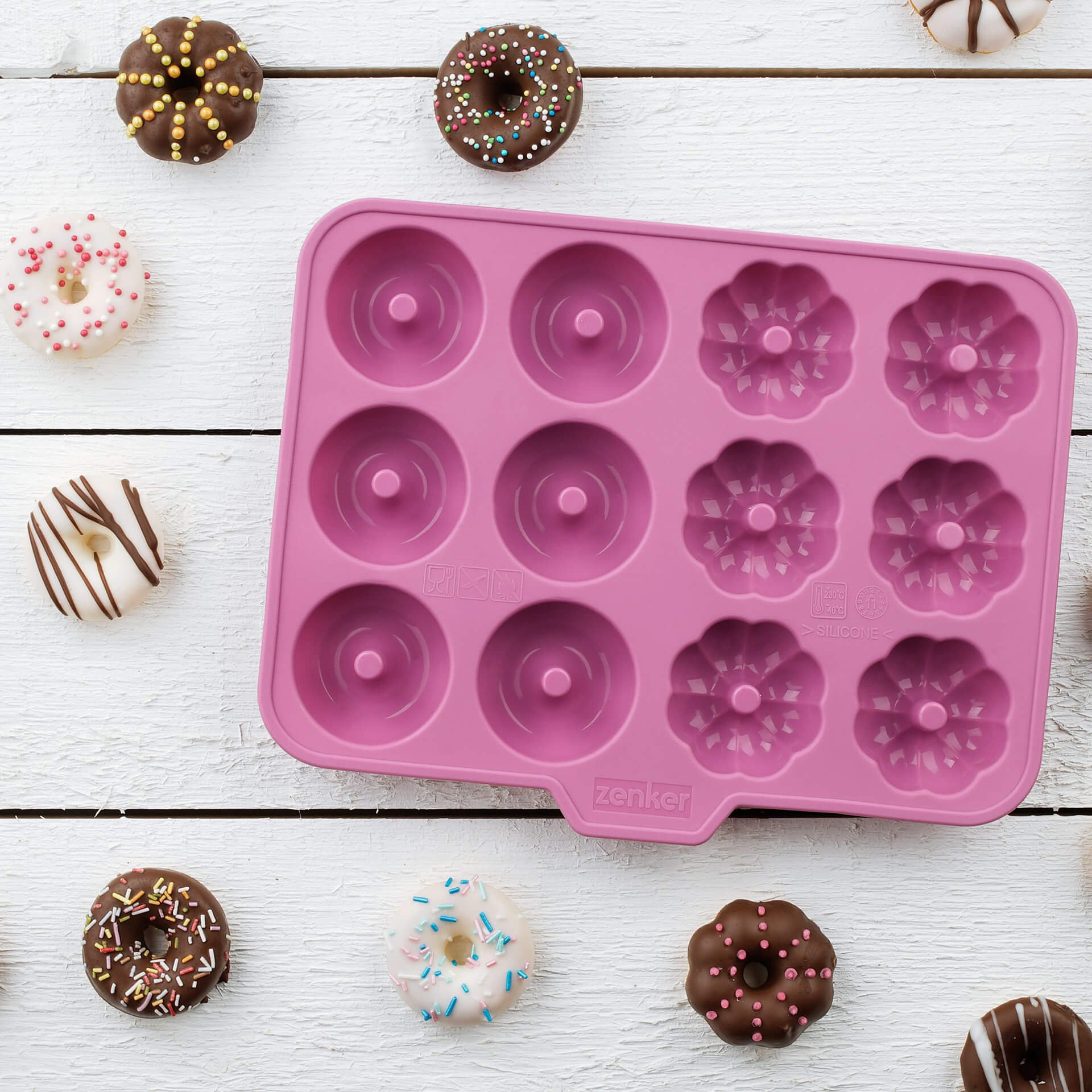 Ein rosa Donut-Backblech mit verschiedenen Donuts auf weißem Holz.