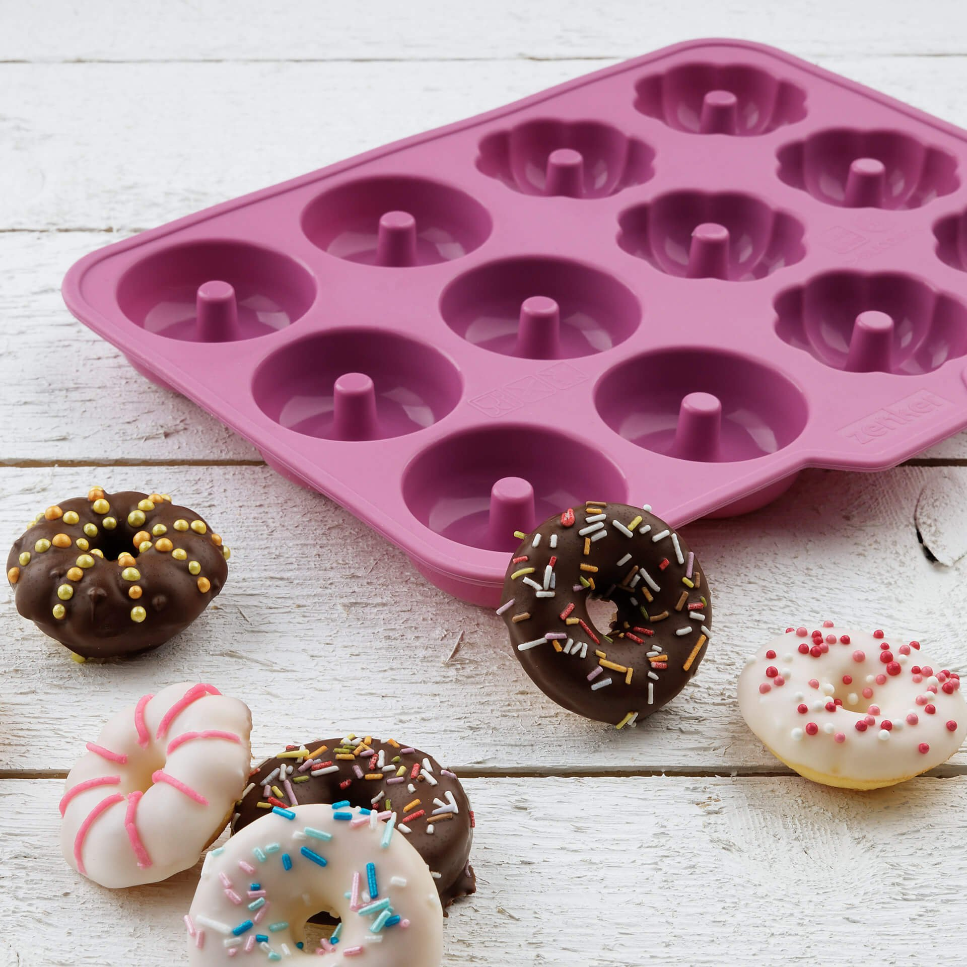 Ein lila Donut-Backblech aus Silikon mit mehreren Mulden und vier verzierten Donuts.