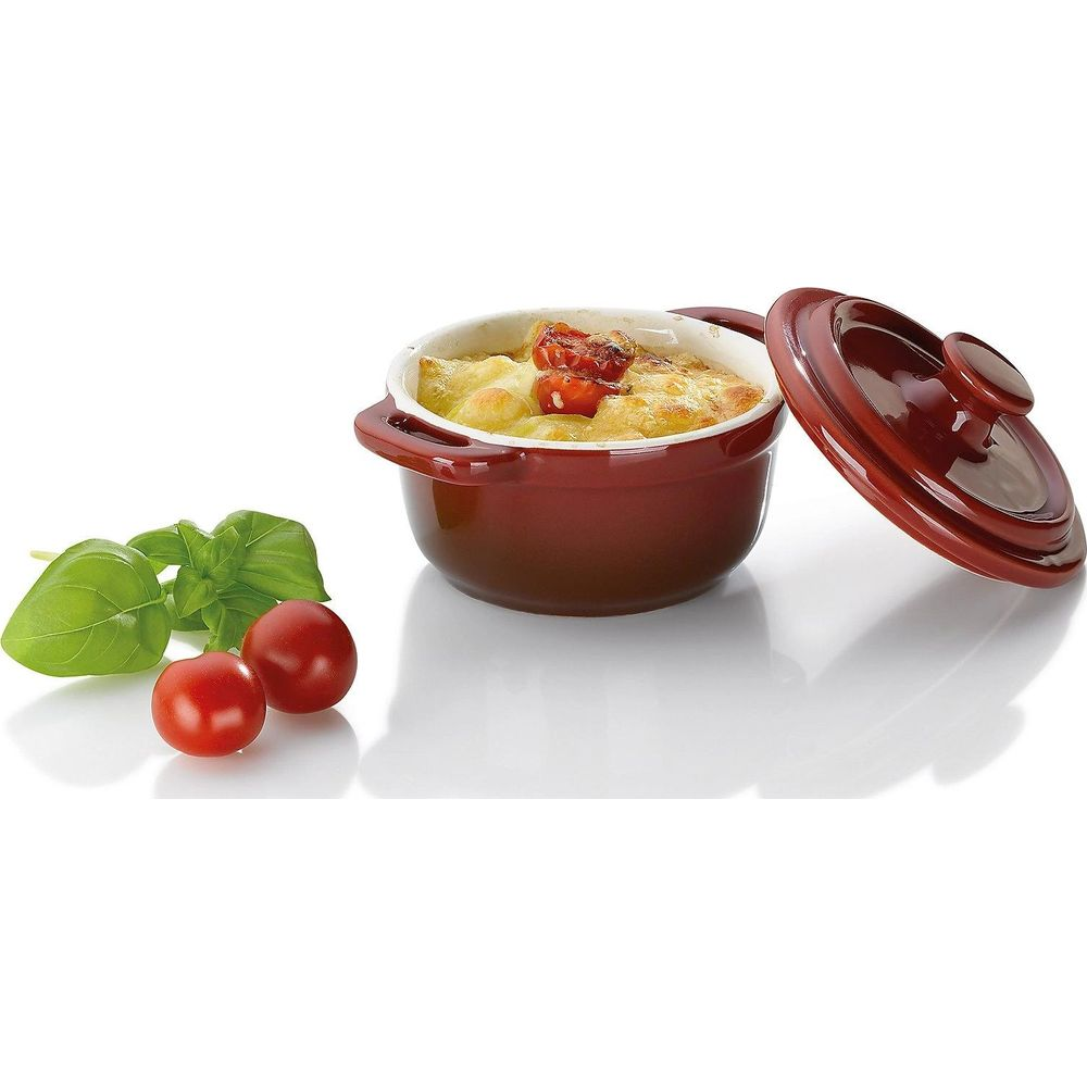 Brauner Auflauf mit Käse und Tomaten, daneben Basilikum und Kirschtomaten.