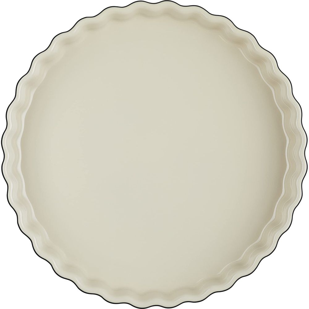 Eine cremefarbene, runde Tarteform mit gewelltem Rand.