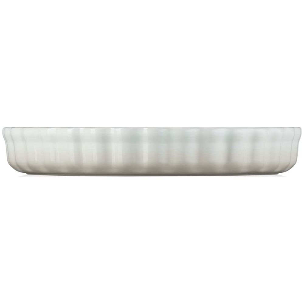 Un plat à tarte en céramique blanc aux bords cannelés.