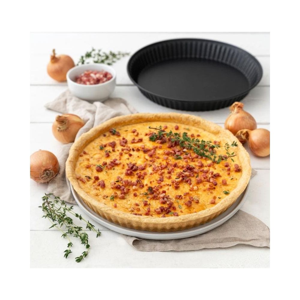 Herzhafter Quiche mit Speck und Zwiebeln, daneben Zwiebeln und ein Backblech.