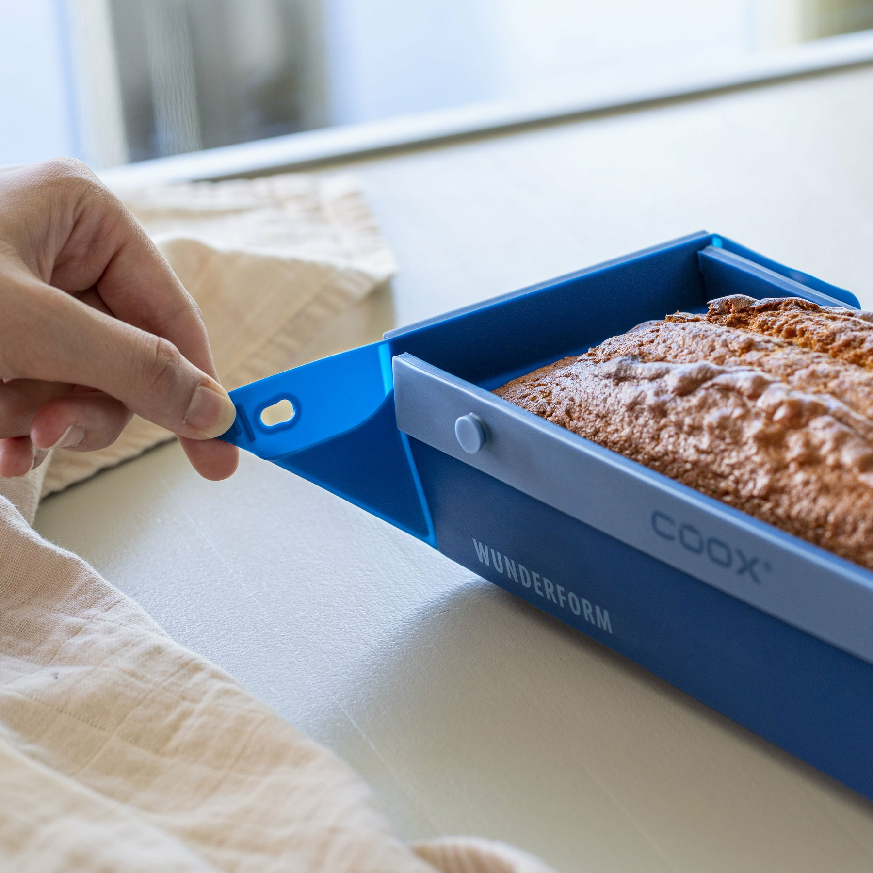 Braune Kuchenform mit Kuchen, die von einer Hand herausgezogen wird.