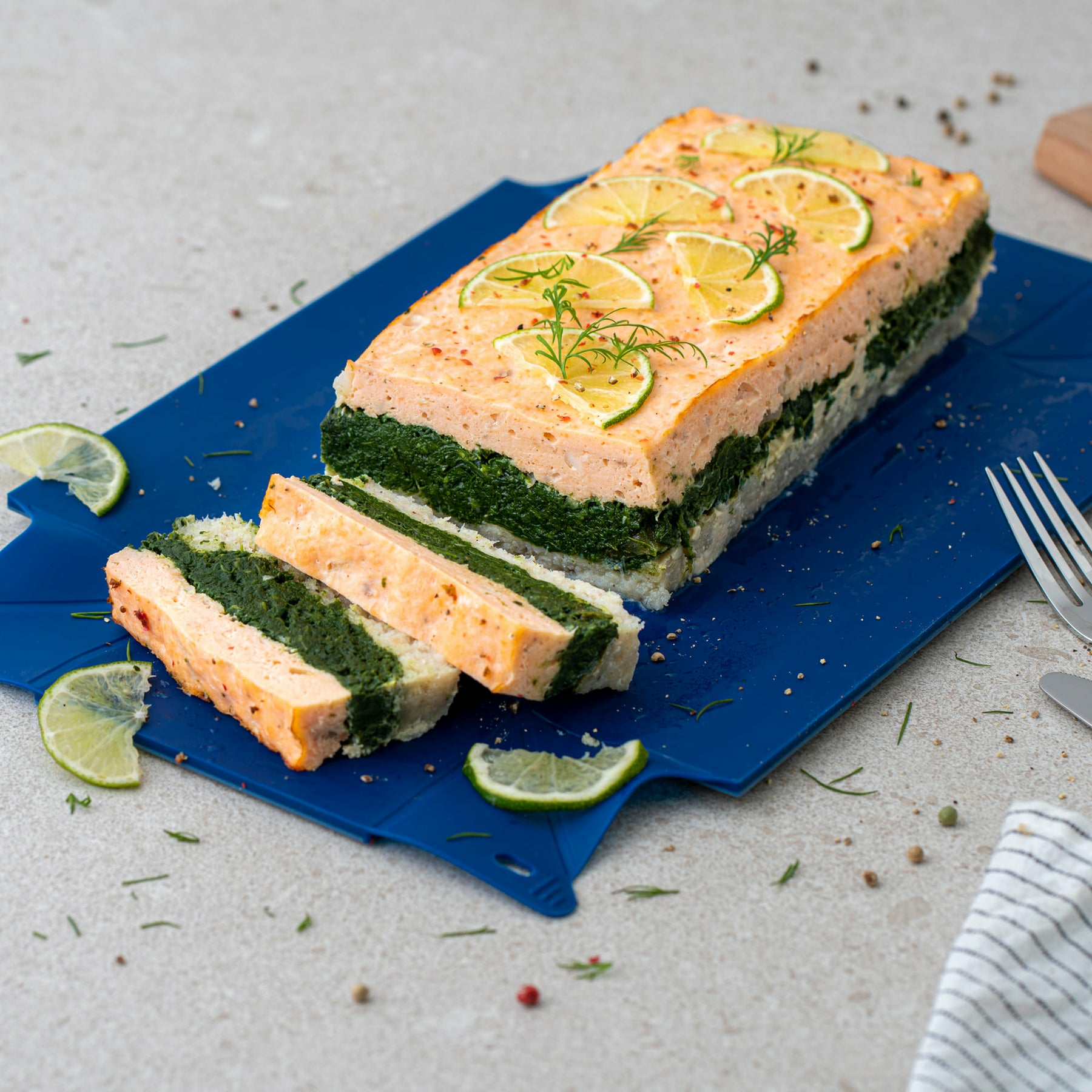 Gefüllter Fischkuchen mit Spinat, garniert mit Limonenscheiben und Dill auf blauem Brett.